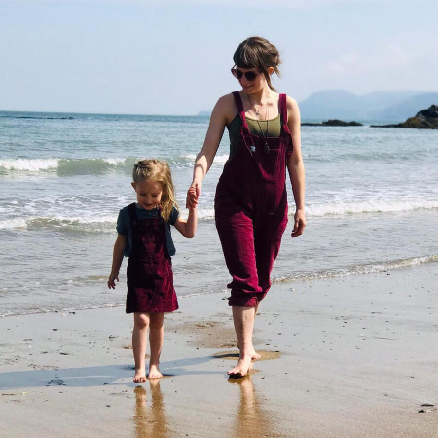 Carli and her daughter holding hands walking barefoot on a beach in Wales