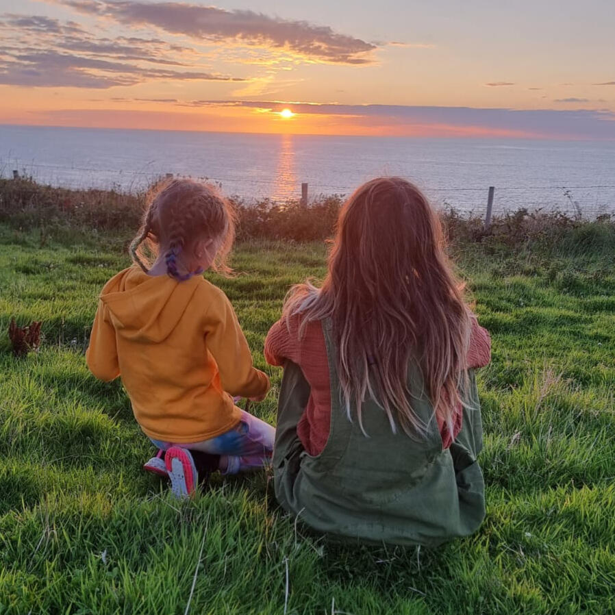 On a Welsh coastal path with my daughter Carli is sitting watching the sun set with her daughter, in a field along a coastal path in Wales